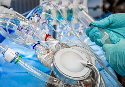 Close-up of laboratory equipment with clear tubes being operated by hands in green medical gloves.