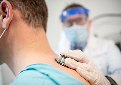 A doctor is putting a stethoscope on a man's back.
